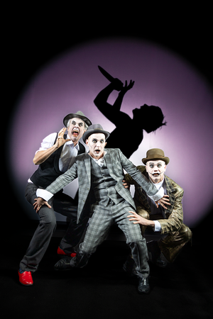 Enrico Petters, Till Schmidt und Florian Krannich tragen Anzüge und sind weiß geschminkt. Sie gucken verängstigt und erschrocken. Im Hintergrund ist ein Schatten einer Person, die singt. © Julia Fenske