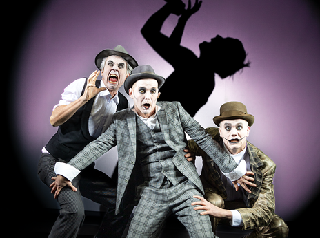 Enrico Petters, Till Schmidt und Florian Krannich tragen Anzüge und sind weiß geschminkt. Sie gucken verängstigt und erschrocken. Im Hintergrund ist ein Schatten einer Person, die singt.