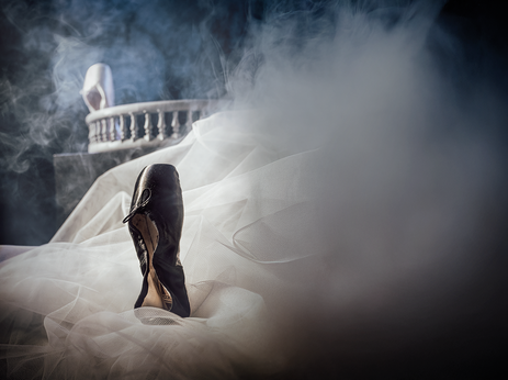 Ein schwarzer Ballettschuh steht auf weißem Tüll. Das Bild ist voller Rauch.
