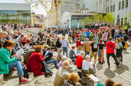 Viele Menschen sitzen auf den Treppen zwischen Universitätsplatz und Kulturinsel, stehen davor, haben Liedtexte in der Hand und schauen zur Bühne auf der Musiker*innen und ein Maibaum stehen. © Anna Kolata