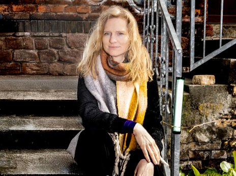 Mille Maria Dalsgaard sitzt auf einer Treppe vor einer Backsteinwand und schaut selbstbewusst in die Kamera.