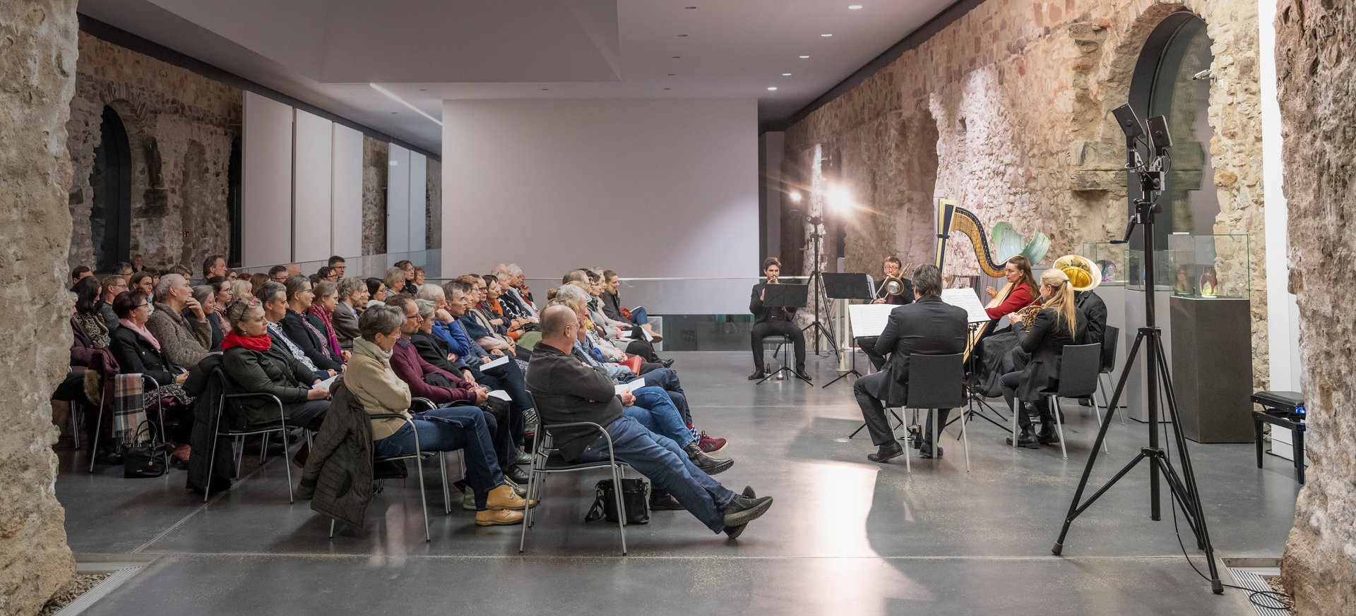 Galeriekonzert in historischem Saal im Kunstmuseum Moritzburg Halle mit Publikum und Ensemble, darunter Harfe, Horn und Klarinette, vor rustikaler Steinwand.