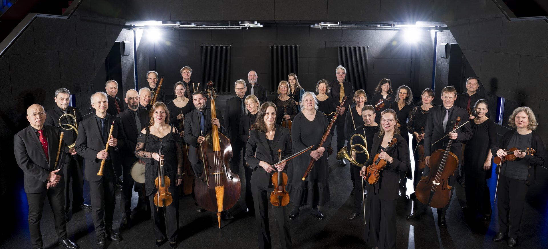 Die Mitglieder des Händelfestspielorchesters stehen mit ihren Instrumenten vor einem schwarzen Hintergrund.
