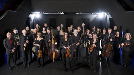 Die Mitglieder des Händelfestspielorchesters stehen mit ihren Instrumenten vor einem schwarzen Hintergrund. © Falk Wenzel