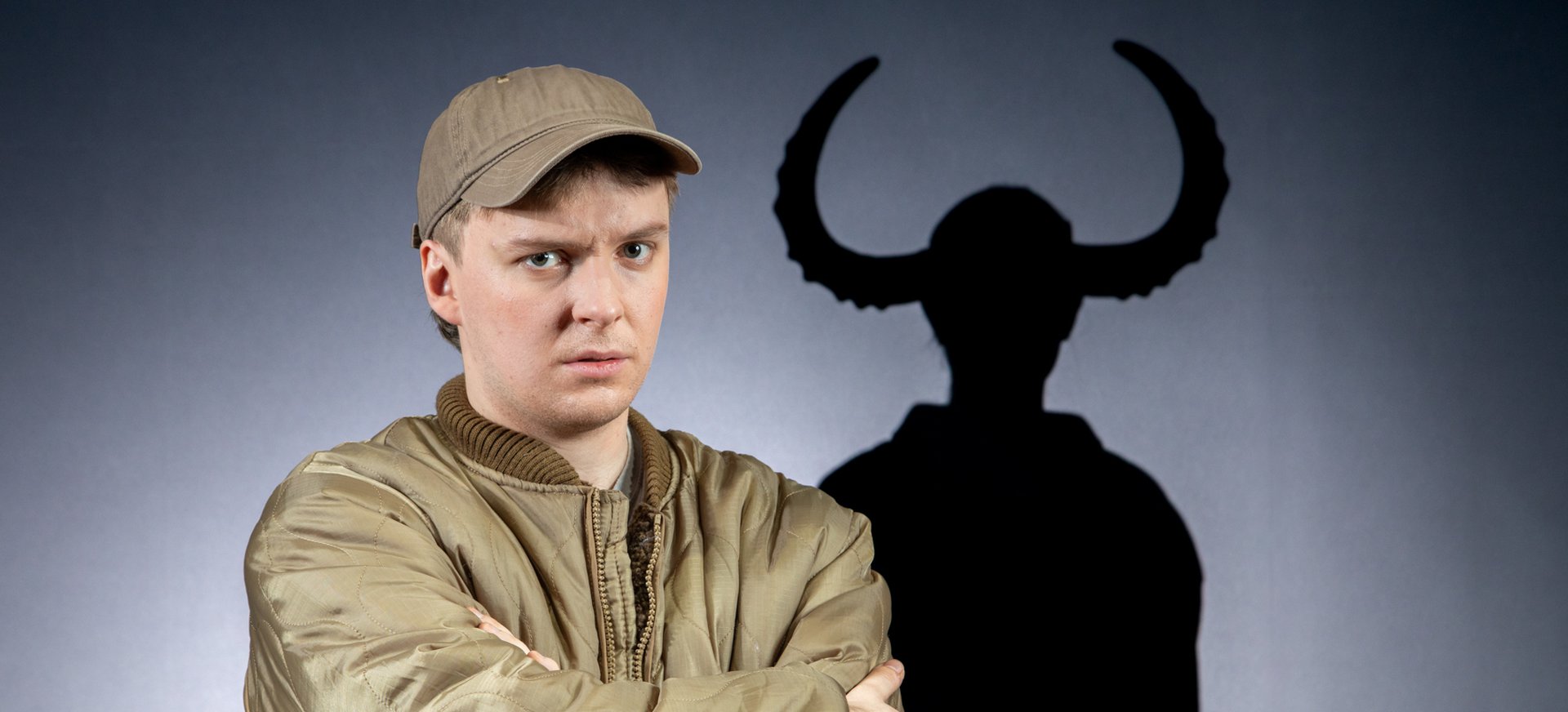 Franz Blumenstock sitzt in Gummistiefeln auf dem Boden. Er guckt verärgert. Im Hintergrund sind Schatten von einem Kind mit Hörnern.