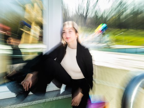 Schauspielerin Kinga Schmidt sitzt außen auf einem Fensterbrett, hat ein Bein darauf aufgestellt und schaut selbstsicher in die Kamera.
