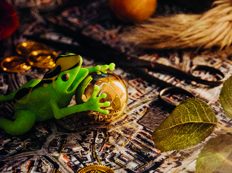 Grüner Spielzeugfrosch umklammert eine goldene Kugel auf einem Stadtplan, umgeben von Goldmünzen, Äpfeln und Blättern.
